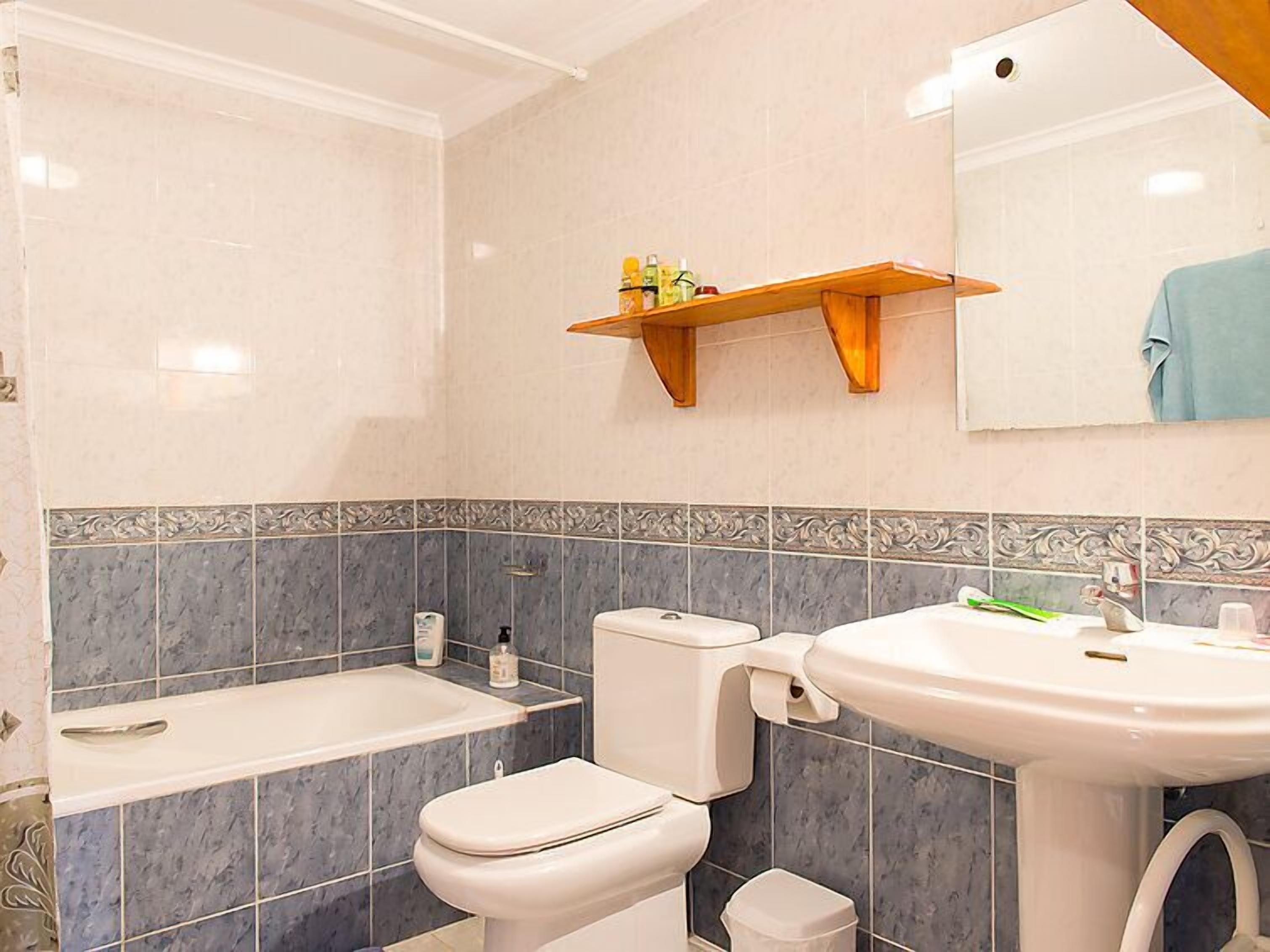A bathroom with a bathtub, toilet, and sink, with a shelf above the toilet holding toiletries.