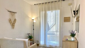 Una camera accogliente con un letto, un tavolino con una ciotola di frutta, una lampada e una finestra vista balcone.