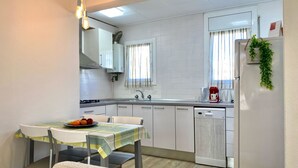 Una cucina compatta con mobili bianchi, un tavolo con sedie, un frigorifero e una macchina da caffè.
