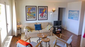 Una sala de estar con un sofá color beige, dos carteles enmarcados, un mueble para televisión y una mesa de centro.