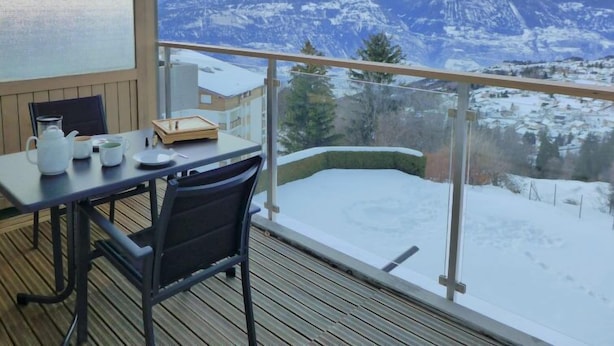 Un balcón con una mesa lista para dos personas, con vistas a un paisaje montañoso nevado.