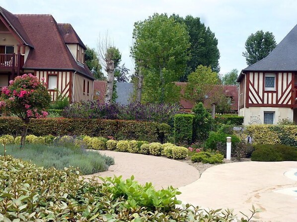 A residential area with traditional half-timbered houses, a well-maintained garden with various shrubs and flowers, and a curved pathway leading through the property.