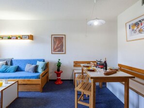 Una sala de estar acogedora con un sofá azul, una mesa de comedor de madera y un taburete rojo.