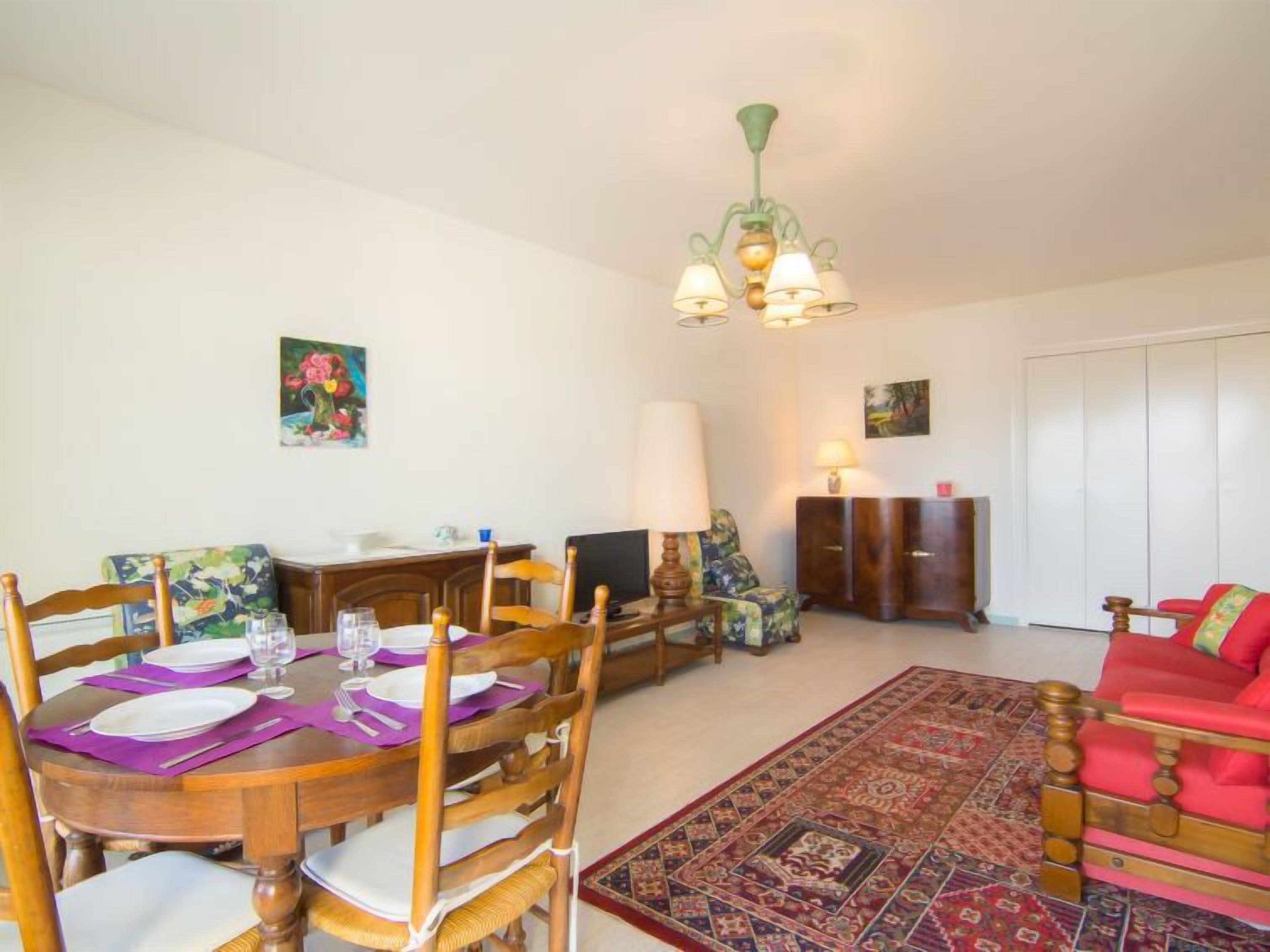 Un coin repas avec une table en bois dressée pour quatre personnes, un canapé rouge et un tapis à motifs.