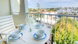Un balcon avec une table préparée pour le thé, des chaises blanches et une vue sur un quartier résidentiel.