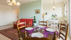Un coin repas avec une table dressée pour quatre personnes, un canapé rouge et, au fond, un espace cuisine.