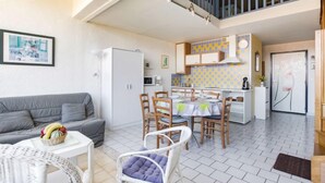 Amplia sala de estar con un sofá gris, una mesa de comedor con sillas, un refrigerador blanco y una cocina con salpicadero de azulejos.