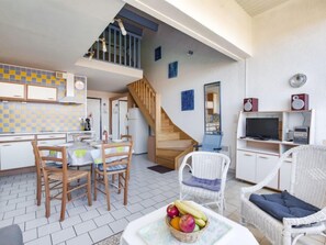 A spacious living area with a dining table, chairs, a wicker sofa, a television, and a staircase leading to an upper level.