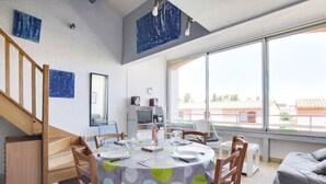 Un comedor moderno con una mesa redonda, sillas de madera y vistas al exterior a través de grandes ventanales.