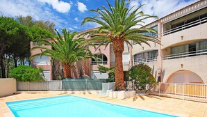 Una piscina con palmeras, un edificio con balcones y un cielo despejado.