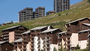 Un conjunto de edificios de varios pisos con balcones, con un paisaje montañoso de fondo.