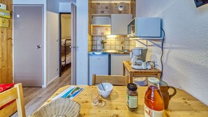 Una cocina compacta equipada con refrigerador, microondas y cafetera. Se aprecia una mesa de comedor con una cesta, un vaso y una botella.