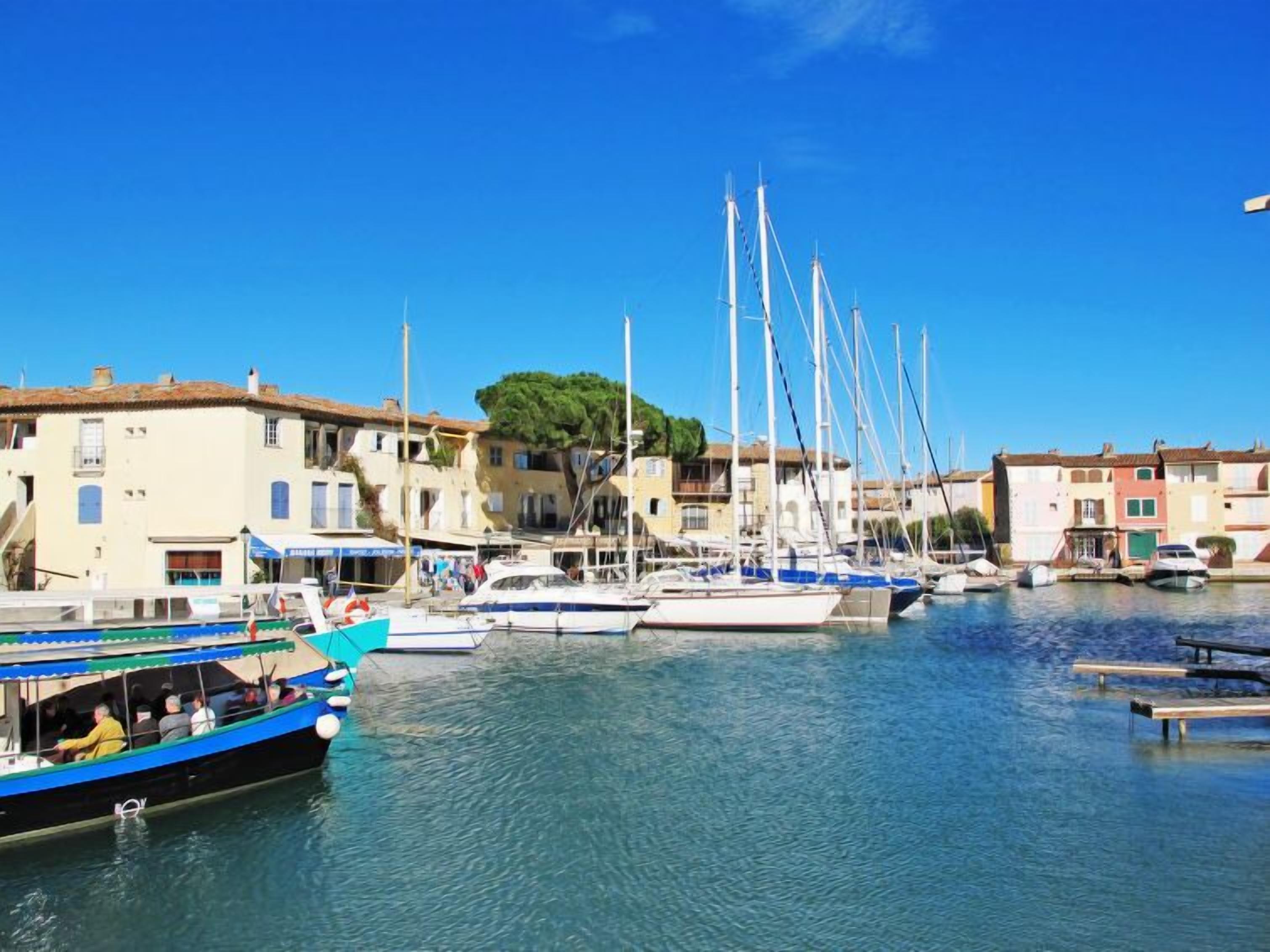 A marina with boats docked, buildings with balconies, and a clear blue sky.