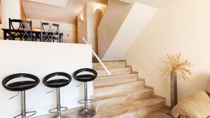 Una cocina moderna con encimera blanca, tres taburetes negros y una escalera que lleva a un nivel superior.