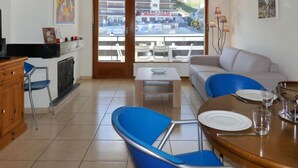 A living room with a sofa, a dining table with chairs, a TV, and a balcony with a view of buildings.