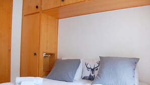 A neatly made bed with white linens, two grey pillows, and a pillow with a deer design.