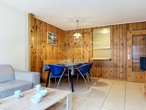 A dining area with a wooden wall, a table set for four, and a sofa in the adjacent room.