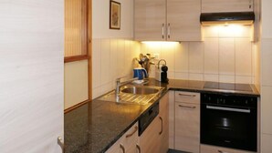 A modern kitchen with light wood cabinets, a stainless steel sink, and a black dishwasher.