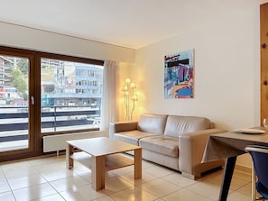 A modern living room with a sofa, a coffee table, and a view of the city through a large window.