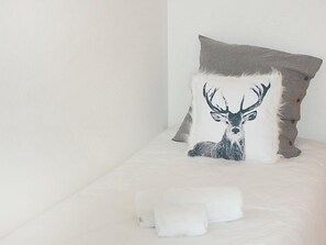 A bed with a pillow featuring a deer design, a grey pillow, and two rolled towels.