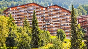 A multi-story hotel with balconies, surrounded by lush greenery and mountains.