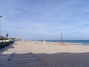A beach with a wooden boardwalk, palm trees, and a clear sky.