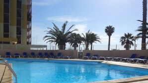A swimming pool with blue water, surrounded by blue lounge chairs and palm trees. - Copacabana by Interhome (Canet-Plage)