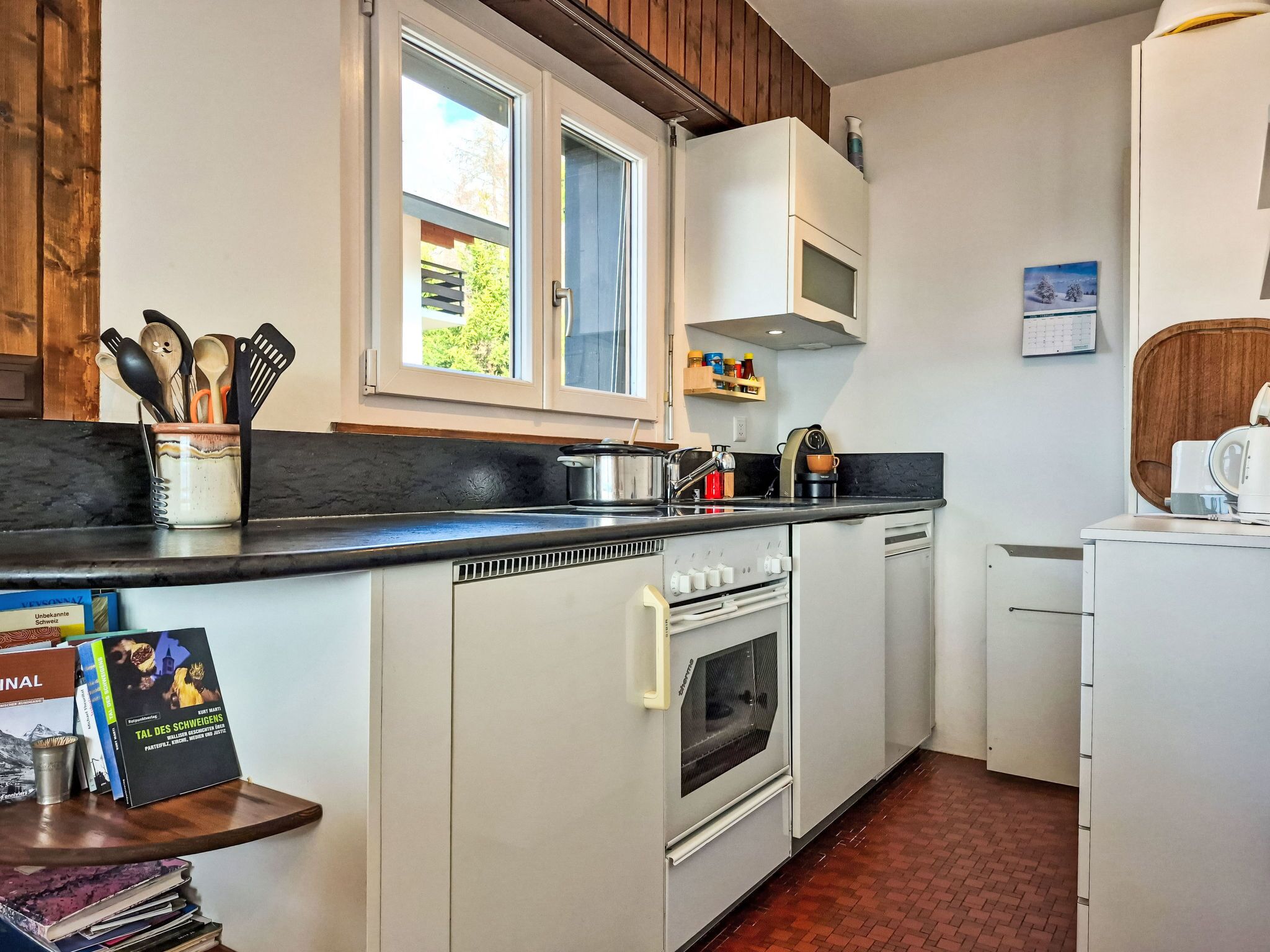 Une cuisine compacte équipée d’une cuisinière, d’un four et d’un évier. Il y a une fenêtre au-dessus de l’évier et un petit réfrigérateur sur la droite.