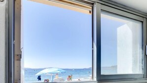 Une fenêtre donnant sur une plage, avec des personnes et un bateau visibles.