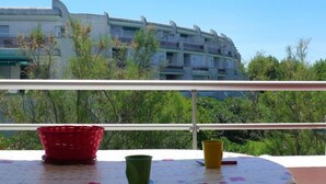 Een balkon met uitzicht op een modern gebouw, een rode mand en een groene beker.