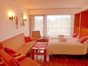 A hotel room with a sofa, two single beds, a chair, a small table, and a window with curtains. - Christiania 2 Tbel by Interhome (Nendaz)