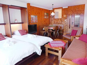 A cozy room with two beds, a TV, a dining table with chairs, and a small seating area. - Christiania 2 Tbel by Interhome (Nendaz)