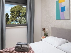 A hotel room with a bed, a window with curtains, a bedside table with a vase and a candle, and a wall with a geometric painting. - Villa Fasana by Interhome (Fažana)