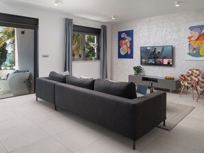 A modern living room with a grey sectional sofa, a flat-screen TV, and a dining area with a patterned chair. - Villa Fasana by Interhome (Fažana)