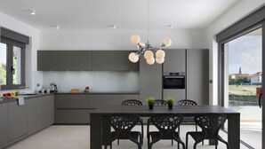Une cuisine moderne dotée d’un îlot central, de meubles de rangement aux couleurs sombres et d’un coin repas avec des chaises.