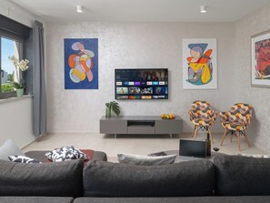 Uma sala de estar moderna com um sofá cinza, uma TV de tela plana na parede e obras de arte abstratas.