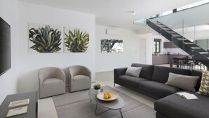 Un salon moderne avec un canapé, deux fauteuils, une table basse sur laquelle on a disposé des fruits, et des œuvres d’art accrochées aux murs.