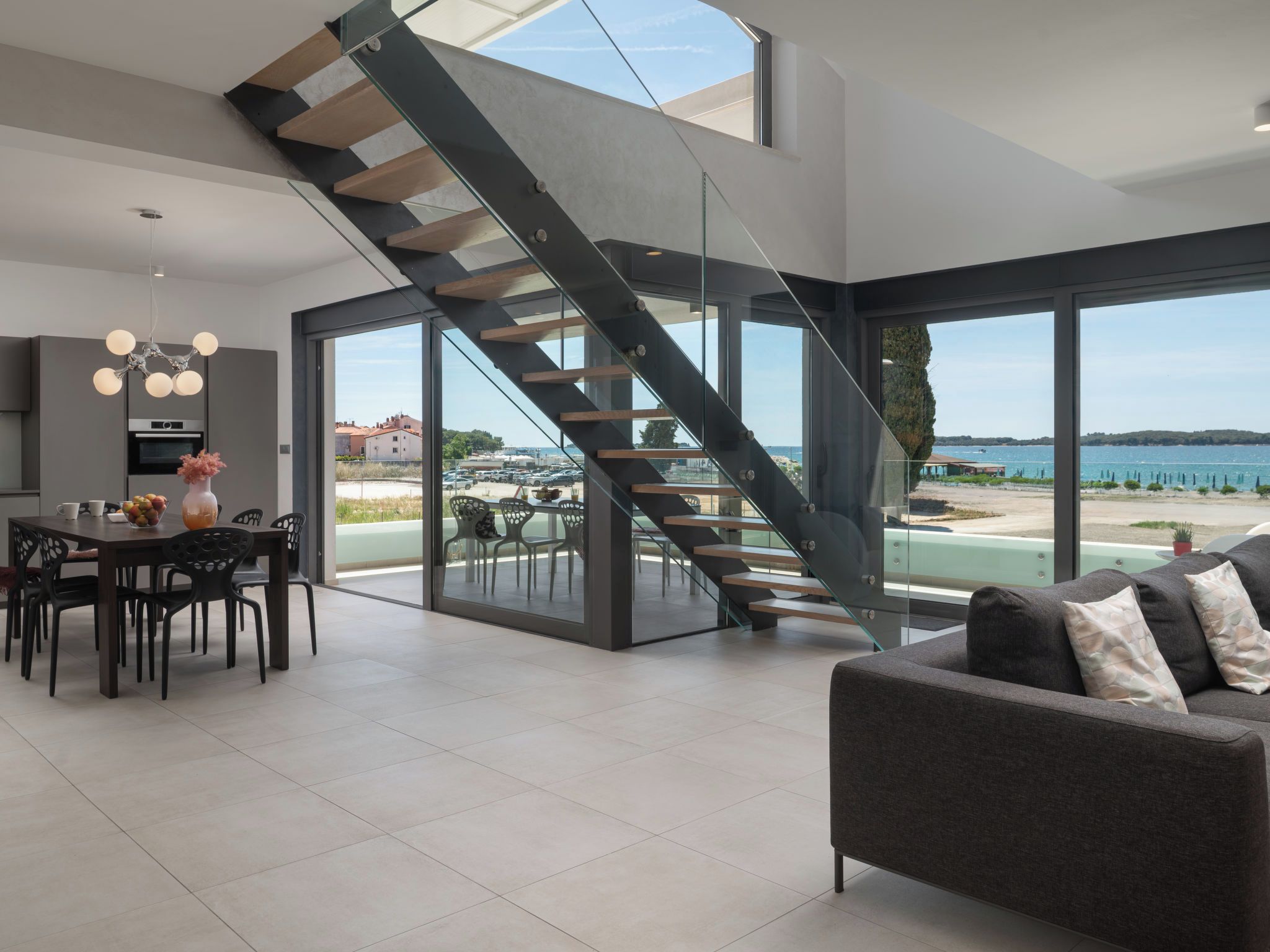 A modern interior with a staircase leading to a balcony overlooking a body of water.