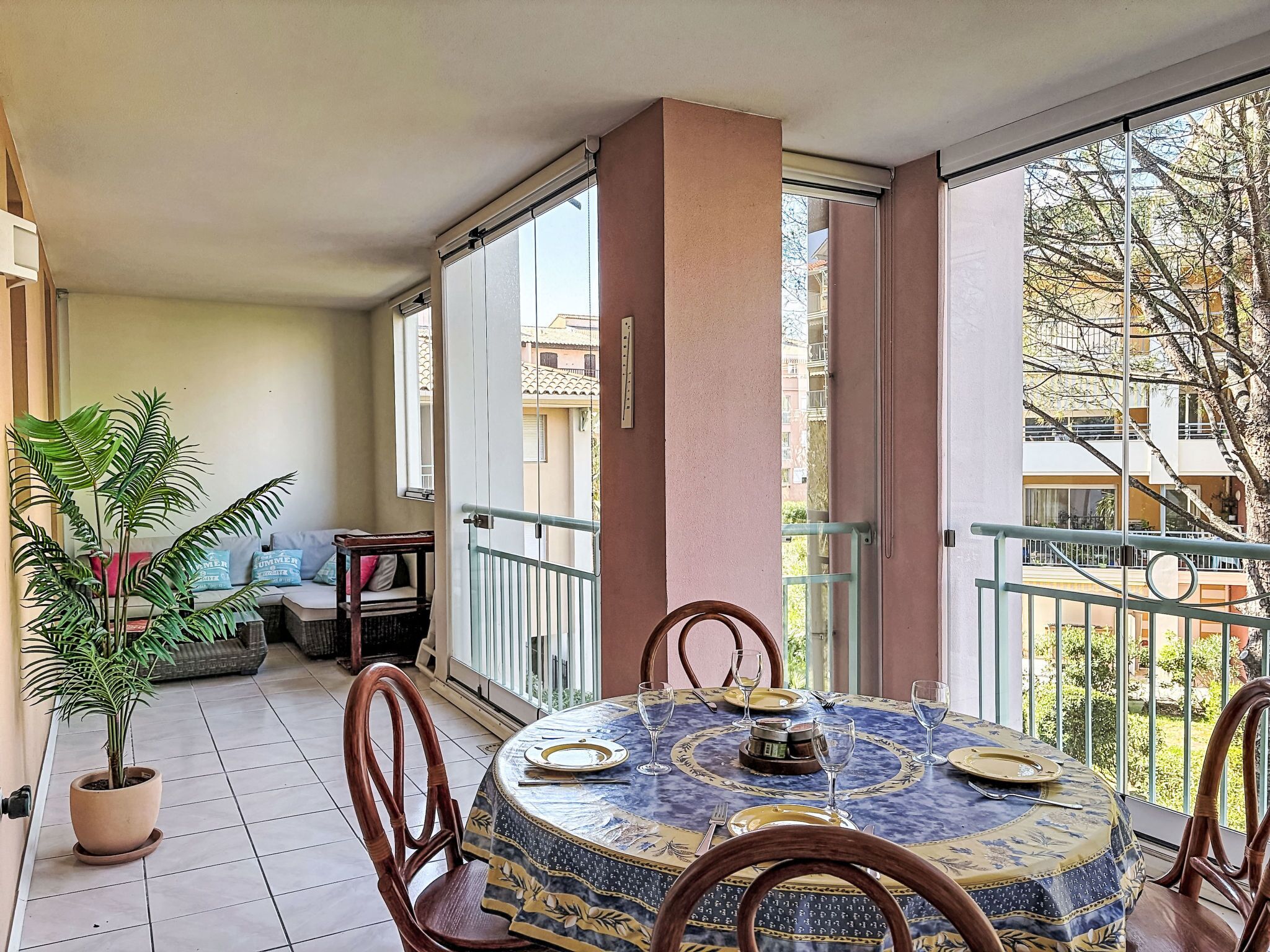 A balcony with a round table set for dining, a potted plant, and a view of neighboring buildings.