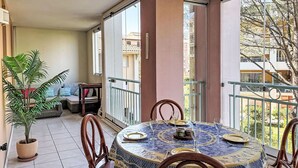 Un balcon avec une table ronde dressée pour le dîner, un pot de fleurs et une vue sur les bâtiments voisins.