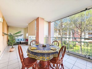 Un balcon avec une table à manger, des chaises et un pot de fleurs.
