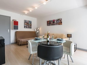 A modern living room with a round dining table, two chairs, a sofa, and a coffee table. There are framed pictures on the wall and a lamp on a side table.