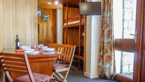 Een gezellige kamer met een houten eettafel gedekt voor twee personen, een stapelbed, een flatscreen-tv en een raam met gordijnen.