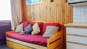 Een kamer met houten lambrisering, een slaapbank van hout, een kitchenette met een magnetron en een raam met gordijnen.