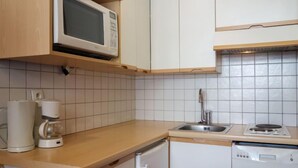 Een keuken met witte kastjes, een magnetron, een koffiezetapparaat, een spoelbak en een vaatwasser.