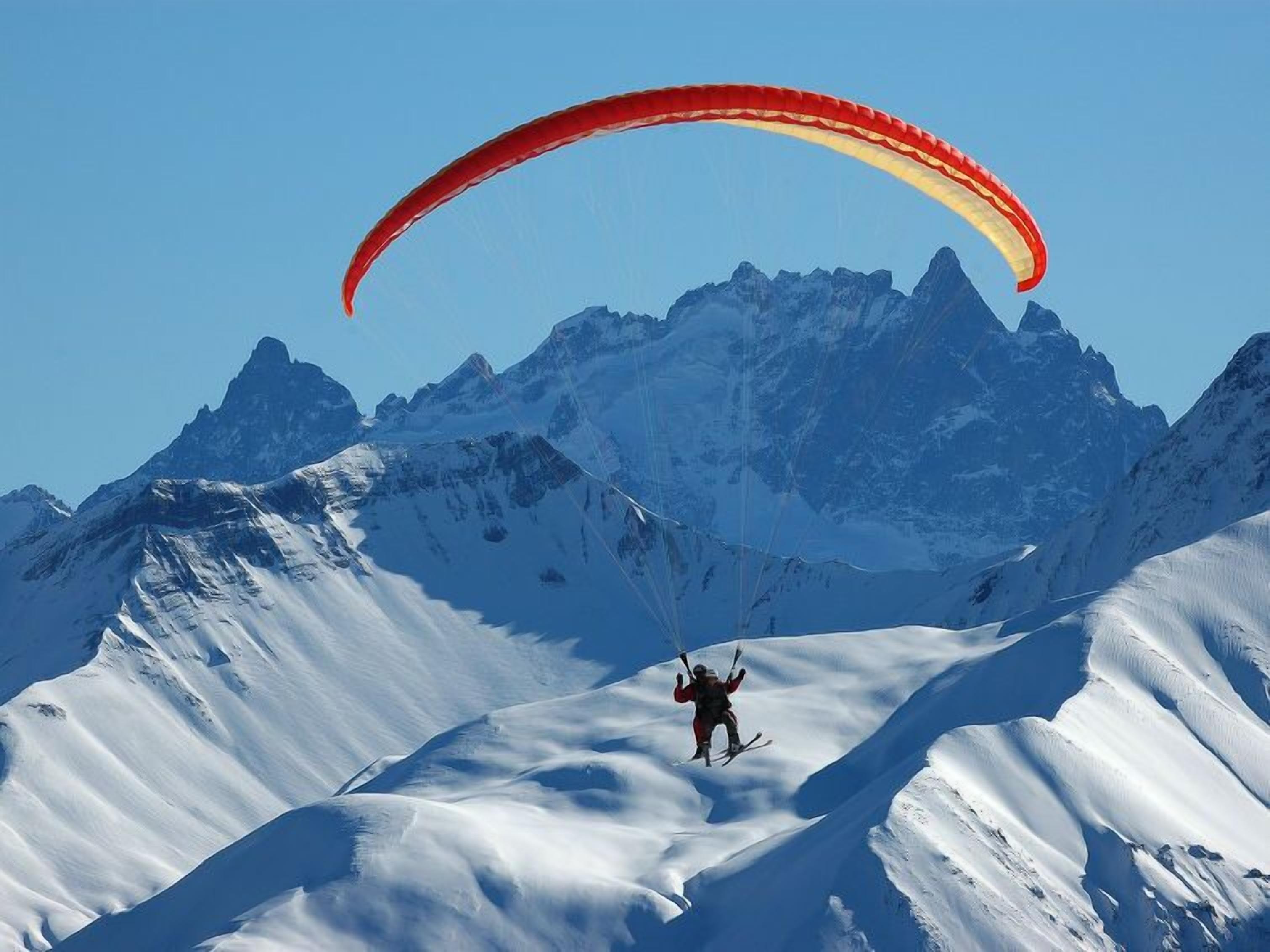 A person paragliding over a snowy mountain landscape with clear blue skies.