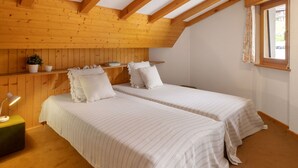 A room with two beds, wooden beams, a window, and a small table with a lamp. - Eldorado 321 by Interhome (Verbier)