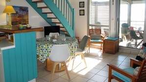 A dining area with a table set for four, a staircase with teal railings, and a view of the outside through a glass door. - Horizon by Interhome (Mimizan)