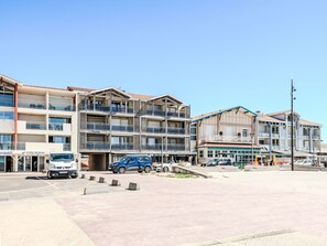 A multi-story building with balconies, a parking area, and various storefronts. - Horizon by Interhome (Mimizan)
