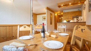 Une table de salle à manger en bois, avec des chaises, une bouteille de vin et des assiettes préparées pour le repas.